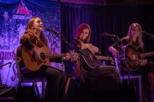 SJ McDonald singing in the foreground with Marti Dodson and Autumn McEntire listening in the background.