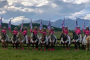 Latigos Up Drill Team The Latigos Up Drill Team wearing matching pink uniforms performs at a Gunnison Tough Enough to Wear Pink event on horseback with flags.