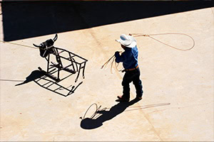 Rodeo Youth Games A little buckeroo in a cowboy hat and boots practices roping on a metal steer.