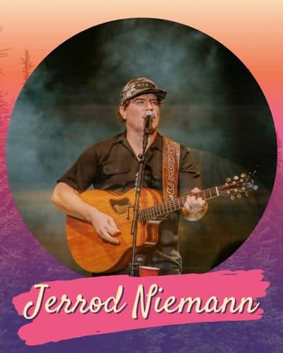 Jerrod Niemann in a brown cowboy shirt playing a guitar and singing on a misty stage.